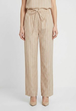 Pantalon large beige à rayures verticales avec une taille à cordon, porté avec des chaussures à talons beiges sur un fond uni.