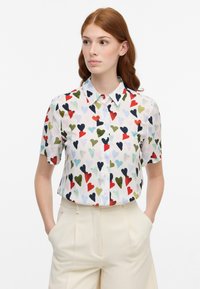 Camicia a maniche corte con bottoni in tessuto leggero e trasparente, caratterizzata da un motivo a cuori multicolore su sfondo bianco.