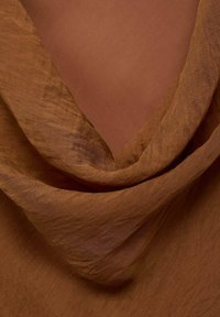 Brown, lightweight fabric with a soft, textured appearance, draped in gentle folds against a solid, darker brown background.