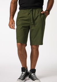 Grüne Baumwollshorts mit einem elastischen Bund und Kordelzugdetail, ausgestattet mit Seitentaschen und einem geraden Schnitt, kombiniert mit schwarzen High-Top Sneakern.