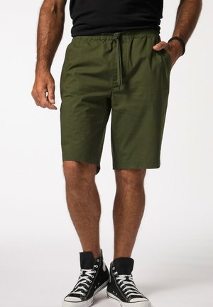 Green cotton shorts with an elastic waistband and drawstring detail, featuring side pockets and a straight cut, paired with black high-top sneakers.