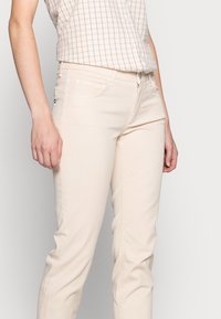 Pantalones ajustados de color beige hechos de mezcla de algodón, con cinco bolsillos, costuras discretas y cintura de tiro medio.