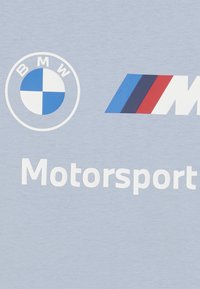 Svijetloplava majica s natpisom BMW roundel loga, M prugama u crvenoj, plavoj i crnoj boji, s natpisom "Motorsport" ispisanim bijelo ispod.