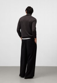 Donkergrijze gebreide trui met een hoge hals, gecombineerd met brede zwarte broek van een gladde stof. De outfit is minimalistisch en ontspannen.