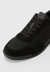 Czarne sportowe buty wykonane z zamszu i siateczki, z płaskimi sznurowadłami, zaokrąglonym czubkiem oraz subtelnym oznaczeniem po bokach i na języku.