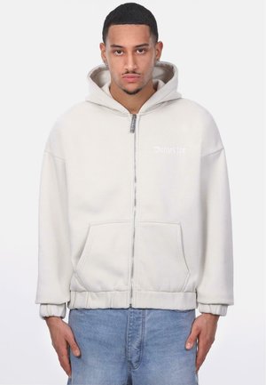 Light gray zip-up hoodie with a kangaroo pocket, elastic cuffs, and drawstring hood. Features subtle logo on the chest. Soft, textured fabric.