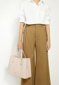 Roze gestructureerde schoudertas met dubbele handvatten, voorzien van een textuur op het oppervlak en gouden hardware accenten. Gestyled met een witte blouse en een paarse broek.