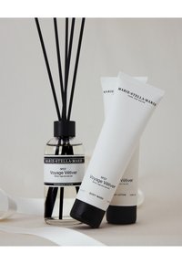 Bâtons de parfum dans un flacon en verre avec un couvercle noir, flanqués de tubes blancs de gel douche et de lotion pour le corps, avec un design d'étiquette minimaliste.