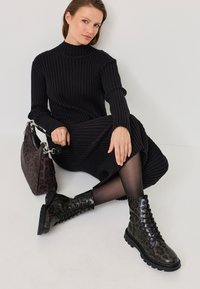 Black ribbed turtleneck dress, paired with knee-high, lace-up leopard print boots and a black leopard print handbag. Textured fabric detail visible.