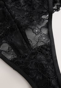 Tissu en dentelle noire avec motifs floraux et sections en maille transparente encadrées par une bordure noire lisse.