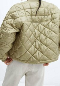 Gevoerde olijfgroene pufferjack met een ruitpatroon, ronde schouders en ribgebreide manchetten. Lichtgewicht stof met een gladde textuur.