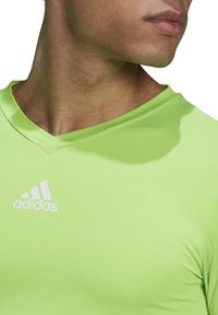 Groene sportieve t-shirt met V-hals ontwerp, gemaakt van soepel, lichtgewicht materiaal met gestructureerde strepen en een wit Adidas-logo.