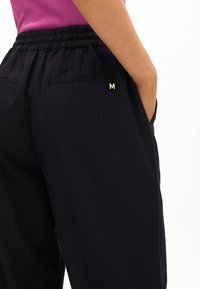 Navy pinstripe housut, joissa on mukava elastinen vyötärö, etutaskut ja pieni kultainen "M"-koriste takana.