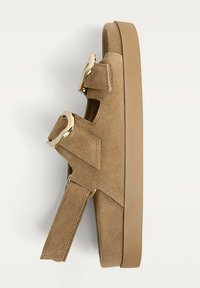 Bruine suède sandalen met een dikke rubberen zool, voorzien van twee verstelbare banden en gouden hardware. Plat ontwerp met uitsparingen.
