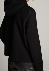 Zwarte hoodie-jack met een losse fit, met een zachte stofstructuur en een cropped ontwerp, zichtbare naden en een capuchon.