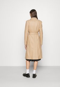 Beige uld trenchcoat med bælte, lange ærmer og en mellemlang længde. Har en ren, skræddersyet silhuet og glat tekstur.