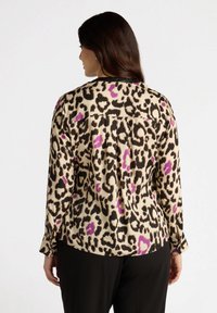 Leopard print blouse in beige, black, and purple. Long sleeves, back pleat detail, and buttoned cuffs. Smooth fabric texture.