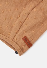 Tecido de cor ferrugem com padrão texturizado de pontos. Apresenta uma etiqueta de couro castanho com "PURE PURE" em relevo. Textura suave e entrelaçada.