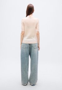 Ανοιχτό ροζ κοντομάνικη πλεκτή μπλούζα με στρογγυλή λαιμόκοψη, συνδυασμένη με φαρδιά, ξεβαμμένα μπλε τζιν παντελόνια με κλασικό σχεδιασμό πέντε τσεπών.