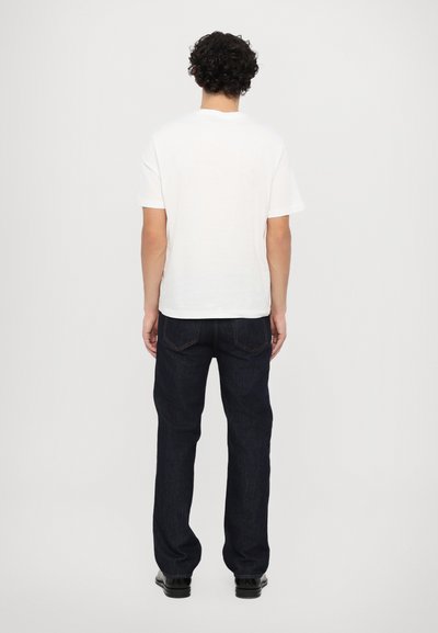 Balta īsām piedurknēm T-kreklu apvienojot ar tumši ziliem džinsiem. Džinsiem ir klasiskā piecu kabatu dizains un nedaudz sašaurinātas kājas.