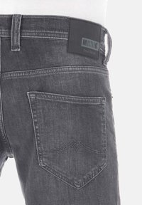 Jeans de mezclilla gris con un diseño ajustado, que cuentan con un parche de cuero negro en la cinta de la cintura y un único bolsillo trasero con costuras distintivas.