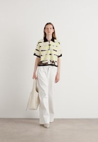 Short-sleeve polo shirt with a black collar, yellow and brown stripes. Paired with loose white trousers and a beige tote bag.
