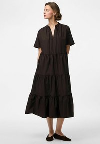 Brūns kokvilnas kleita ar īsām piedurknēm, ar pakāpenisku dizainu, savilktu dekoltē un sānu kabatām. Ceļa garuma, ar brīvu piegriezumu.