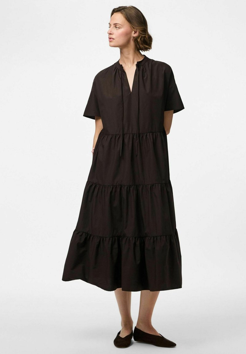 Brūns kokvilnas kleita ar īsām piedurknēm, ar pakāpenisku dizainu, savilktu dekoltē un sānu kabatām. Ceļa garuma, ar brīvu piegriezumu.