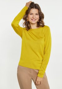 Pulover lung galben cu mânecă lungă, dintr-un material tricotat moale, cu o croială relaxată și decolteu rotund, asociat cu pantaloni bej.
