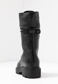 Botte noire en cuir montant jusqu'au genou avec une finition texturée, dotée d'un lacet décoratif sur le côté et d'une semelle en caoutchouc robuste pour une meilleure adhérence.