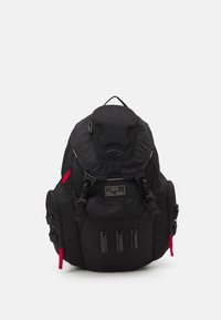 Black backpack made of durable fabric, featuring multiple zippered compartments, padded straps, and red accent details. Brand logo visible.