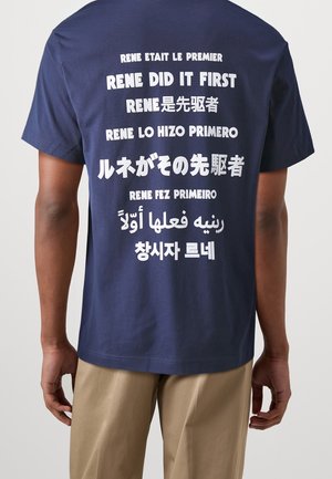 Námořnická modrá bavlněná tričko se silným bílým textem v různých jazycích na zadní straně, s uvolněným střihem a krátkými rukávy.