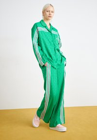 Green patterned matching shirt and pants set with pink and white stripes along the sleeves and sides, paired with light pink sneakers.
