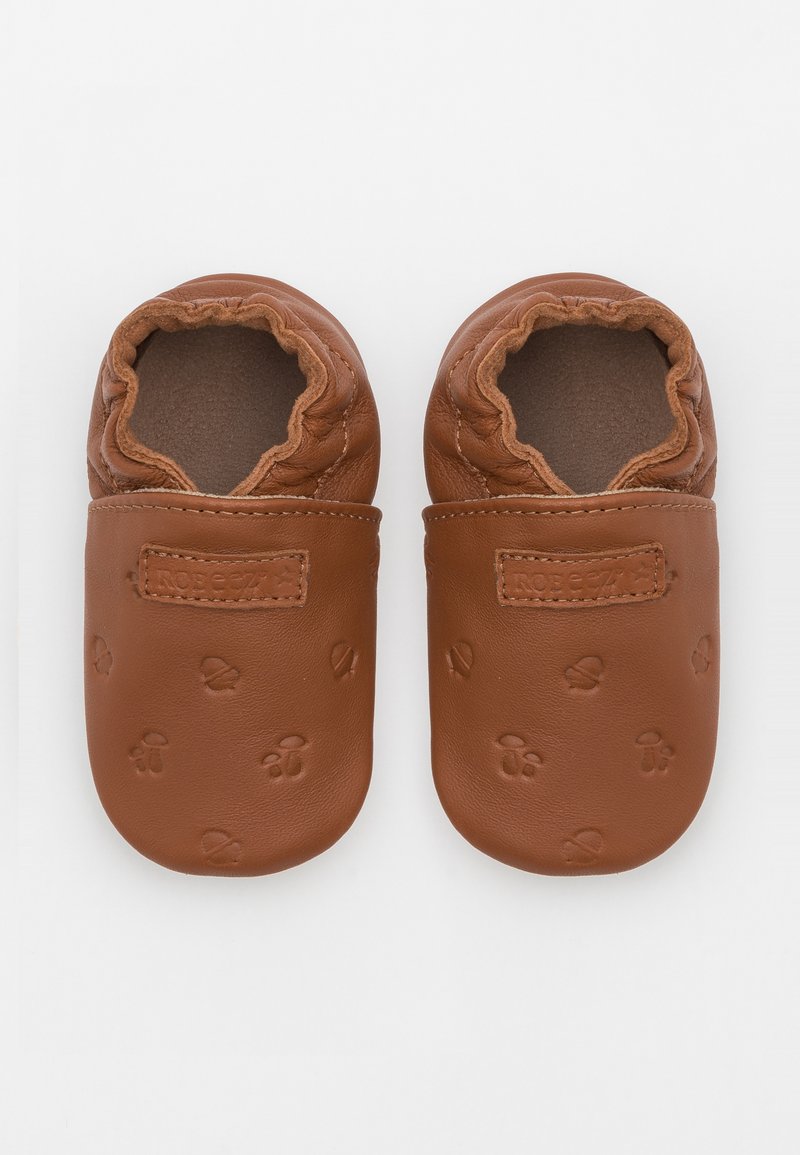 Pantofii de bebeluși din piele maro, cu deschideri elastice, embossati cu modele mici de urme de labe, cu o suprafață texturată și căptușeală moale.