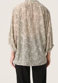 Camicia ampia e trasparente con un motivo geometrico testurizzato in tonalità di verde tenue e beige. Presenta maniche arrotolate e un orlo arrotondato.
