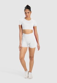 White sportswear set featuring a short-sleeve crop top and high-waisted shorts. Material appears smooth with a fitted design.