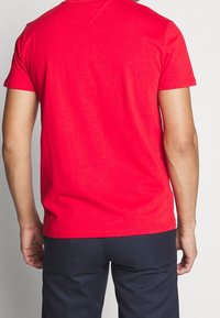 Czerwona bawełniana koszulka z krótkimi rękawami, okrągłym dekoltem i przeszyciami. Noszona z granatowymi spodniami o gładkiej, jednolitej fakturze.