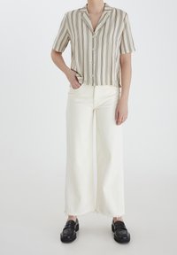 Camicia a maniche corte color crema con righe verticali nere, design con bottoni. Abbinata a jeans bianchi a gamba larga e mocassini neri.