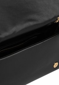 Czarna skórzana torebka z otwartą klapą, odsłaniającą wewnętrzną kieszeń na zamek błyskawiczny oraz złoty zatrzask z magnesem.