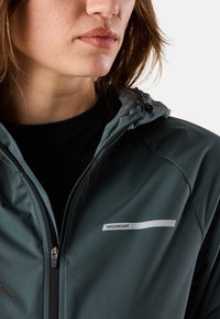 Veste softshell vert foncé avec capuche, dotée d'une fermeture éclair et d'un logo blanc "SWEDMOUNT" à l'avant. Texture de tissu lisse.