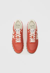 Zapatillas deportivas rojas con parte superior de malla, cordones blancos y suelas de goma. Presentan un logo en la lengüeta y un acento blanco en contraste en el lateral.