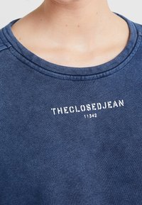 Felpa blu navy con scollo rotondo, caratterizzata da una scritta bianca "THECLOSEDJEAN 11342" sul davanti. Il tessuto sembra morbido e strutturato.