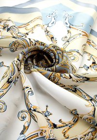 Foulard in seta con una base bianca decorata con motivi ornati blu e oro. Il tessuto ha una consistenza liscia e una caduta elegante.