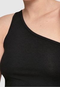 Débardeur noir avec un design à une épaule. Fabriqué dans un tissu lisse et extensible avec une coupe ajustée et un décolleté simple et épuré.