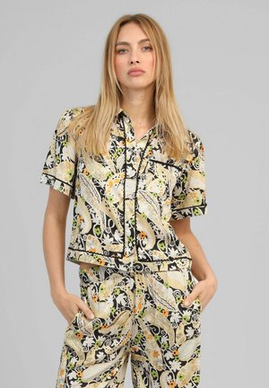Femme aux longs cheveux blonds portant un ensemble assorti composé d'une chemise à manches courtes et d'un pantalon avec un motif coloré paisley et floral.