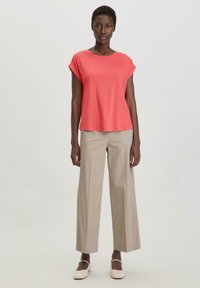 Koraalkleurig T-shirt met korte mouwen, gecombineerd met beige wijde broekspijpen. Zachte textuur, eenvoudig ontwerp en minimale accenten.