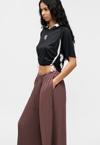 Μαύρο κοντό αθλητικό τοπ με διακριτικό καρό μοτίβο και λευκές πλαϊνές λεπτομέρειες, συνδυασμένο με φαρδιά, πιετετέ καφέ παντελόνια με πλαϊνές τσέπες.