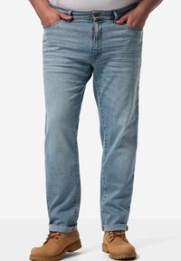 Jeans de mezclilla azul claro con un corte relajado, que cuentan con un cierre de botón y cremallera, y puños enrollados, combinados con botas de trabajo color marrón.