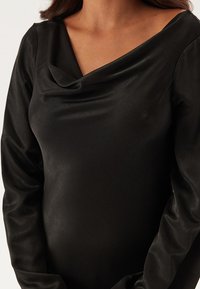 Zwarte satijnen jurk met een coulus-halslijn en lange mouwen, met een gladde textuur en een aansluitend ontwerp dat de silhouet accentueert.