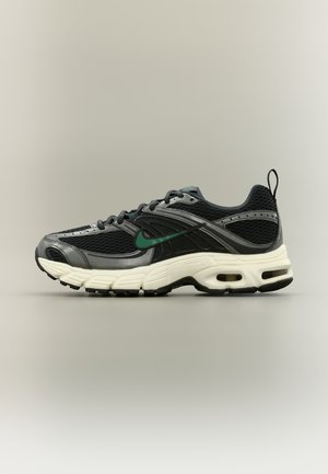 Baskets athlétiques noires et grises avec une tige en mesh, un swoosh Nike vert, une semelle blanche amortissante, des unités d'air visibles et une languette au talon.